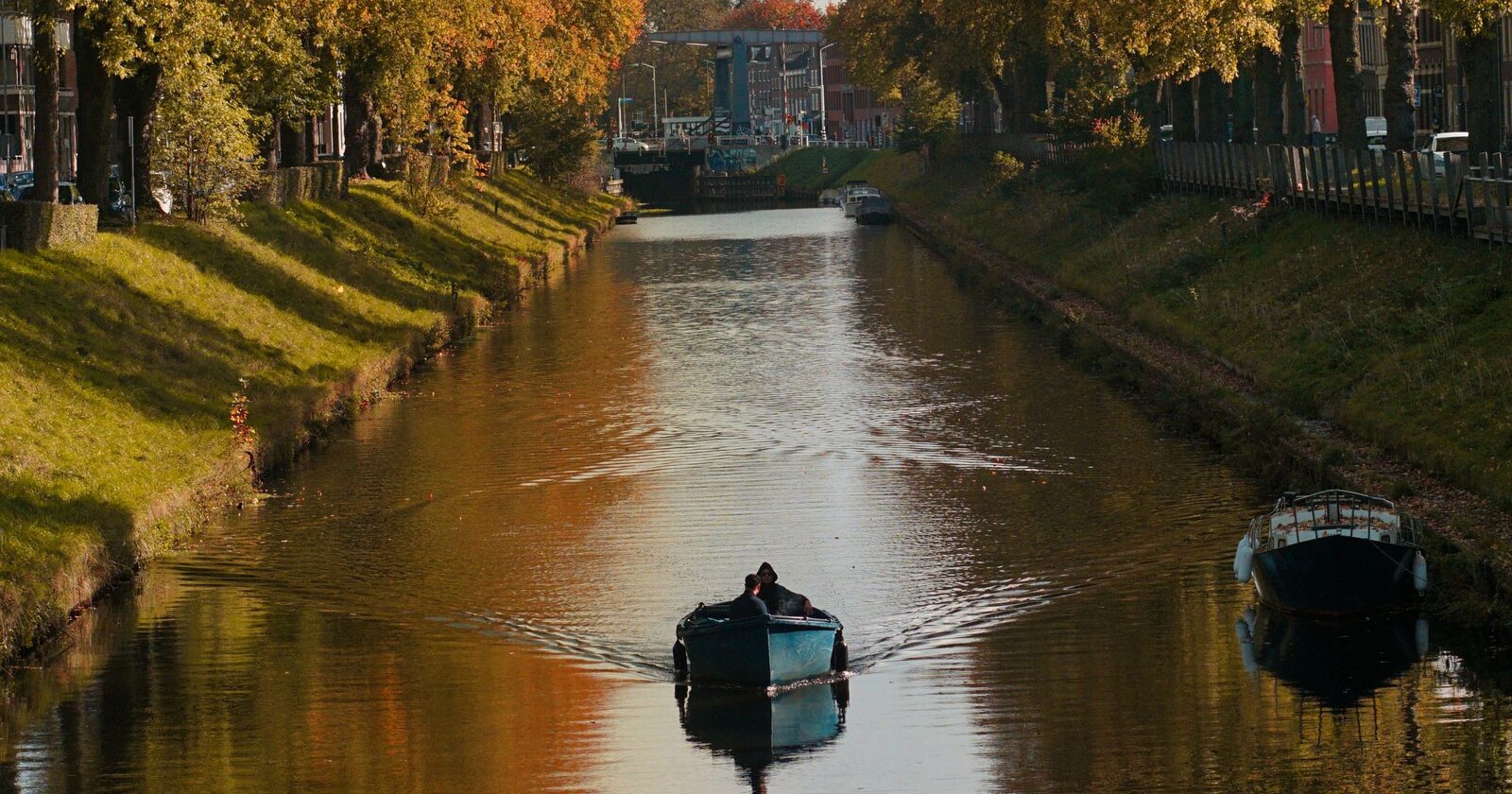 A small boat cruising a calm canal lined with golden autumn foliage and reflections