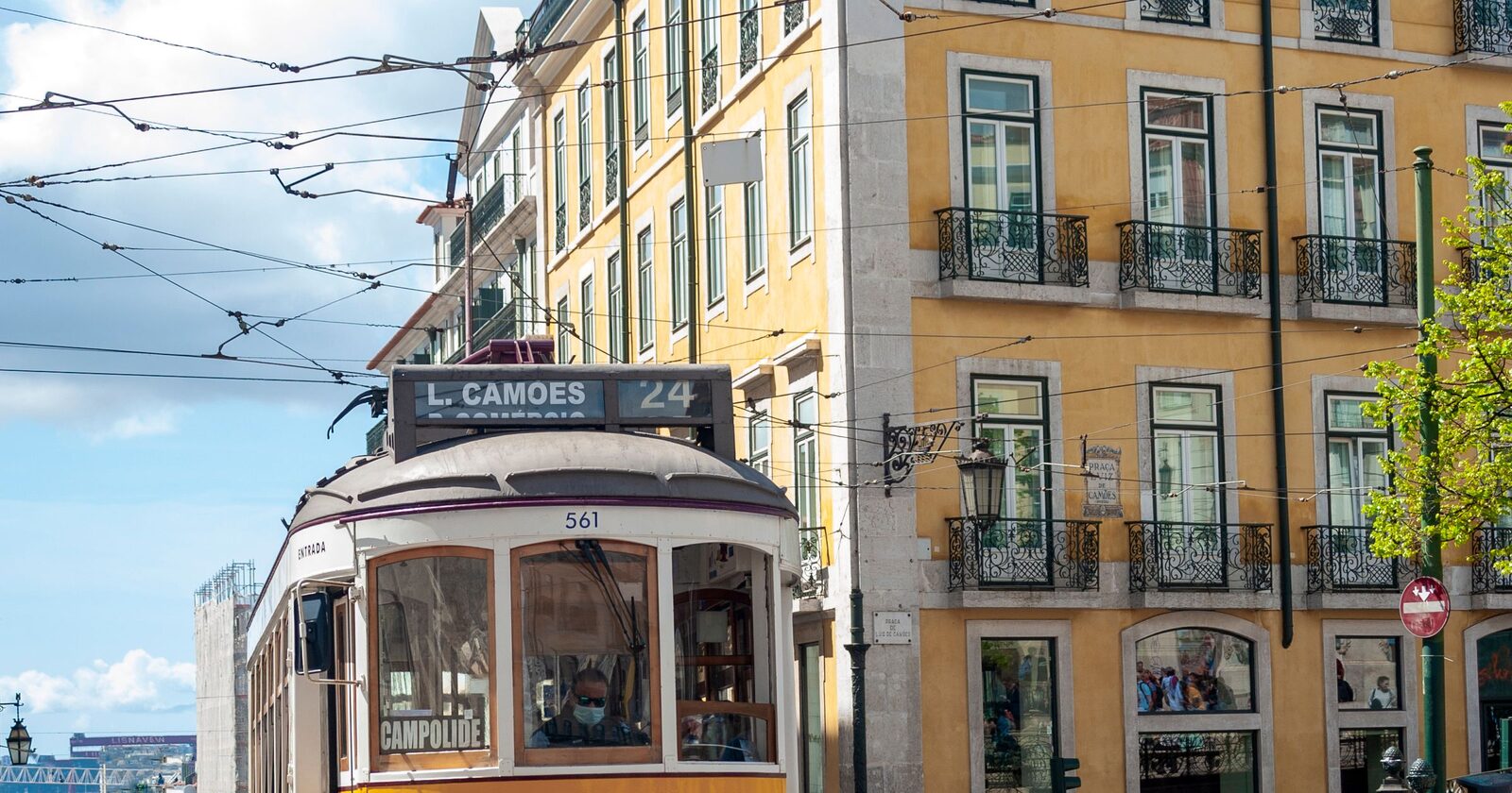 A vintage yellow Lisbon tram passing tiled pastel buildings under a blue sky